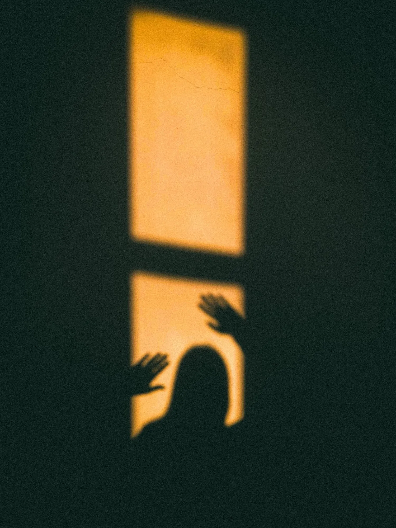 Schatten einer Person im Fensterlicht an einer dunklen Wand